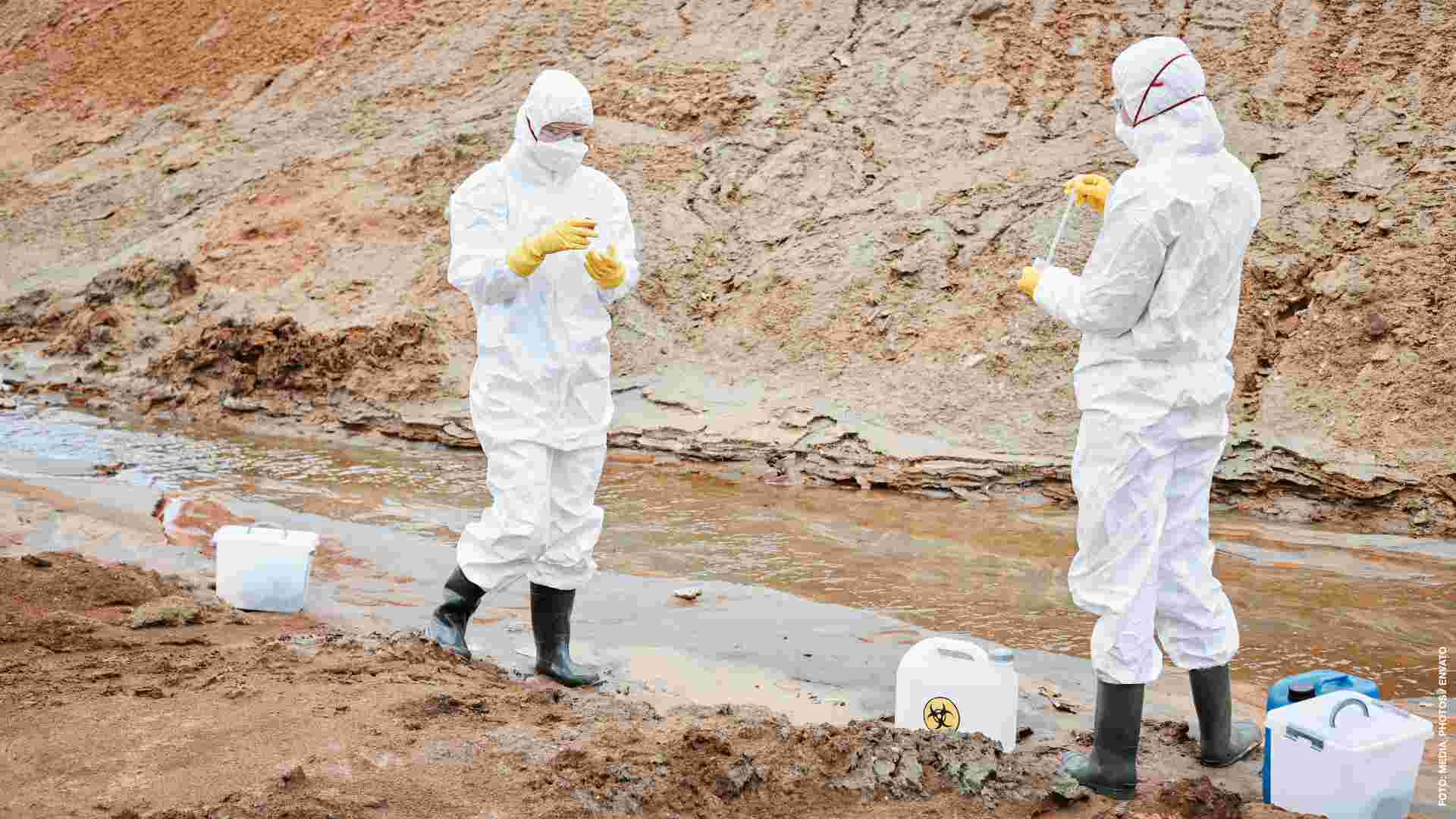 Environmental scientists in masks, gloves and protective suits working with toxic substances on polluted area