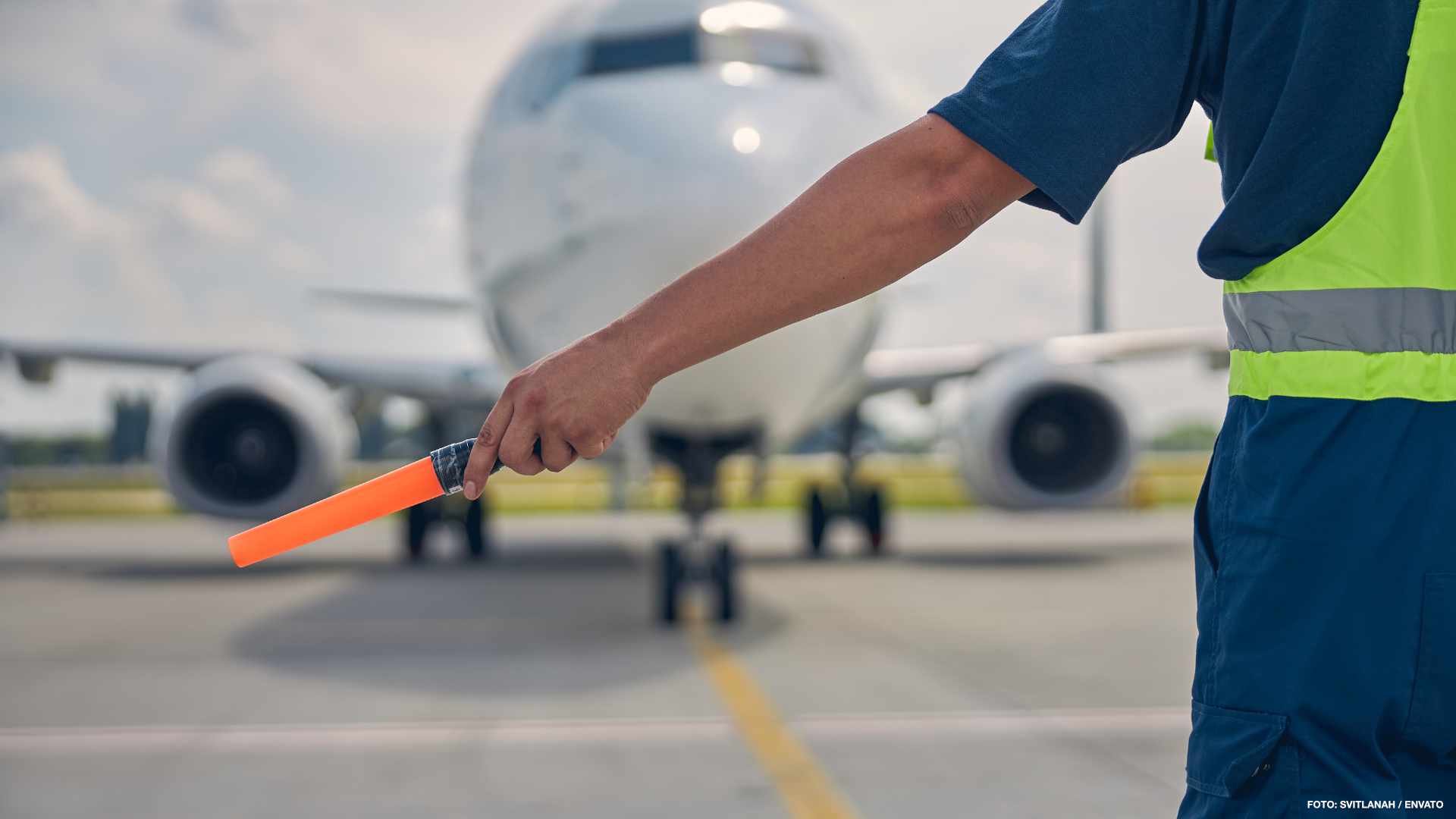 Cropped photo of an airport worker in uniform holding a marshaling wand in one hand