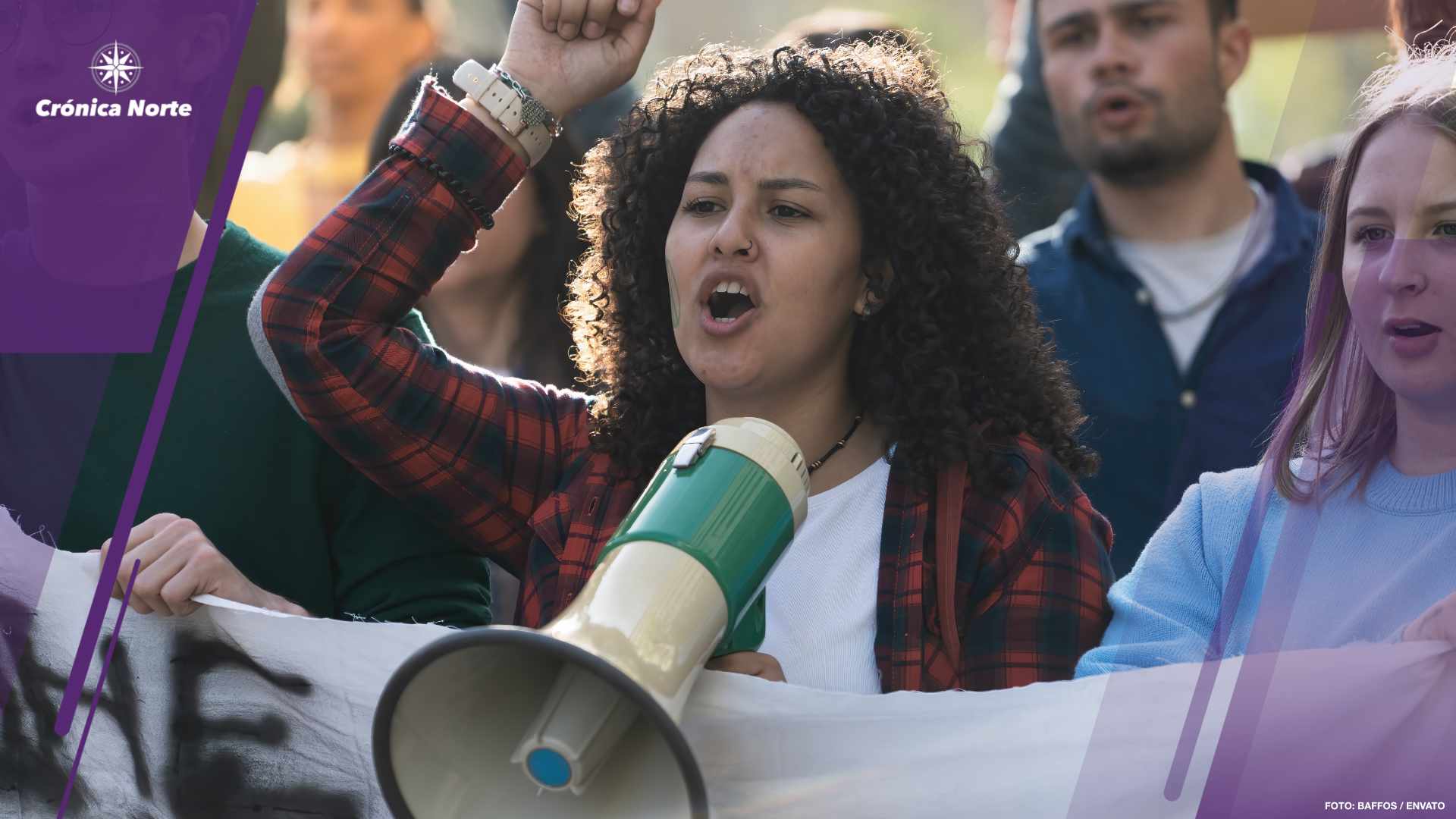 Close-up of a young woman with curly hair, leading a student protest using a megaphone. The group, holding an unidentifiable banner, passionately chants slogans.